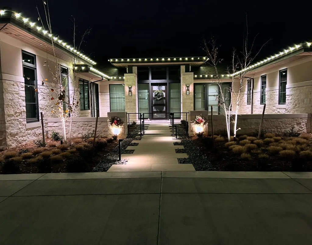 A beautifully lit walkway leads to an elegantly decorated entrance at night
