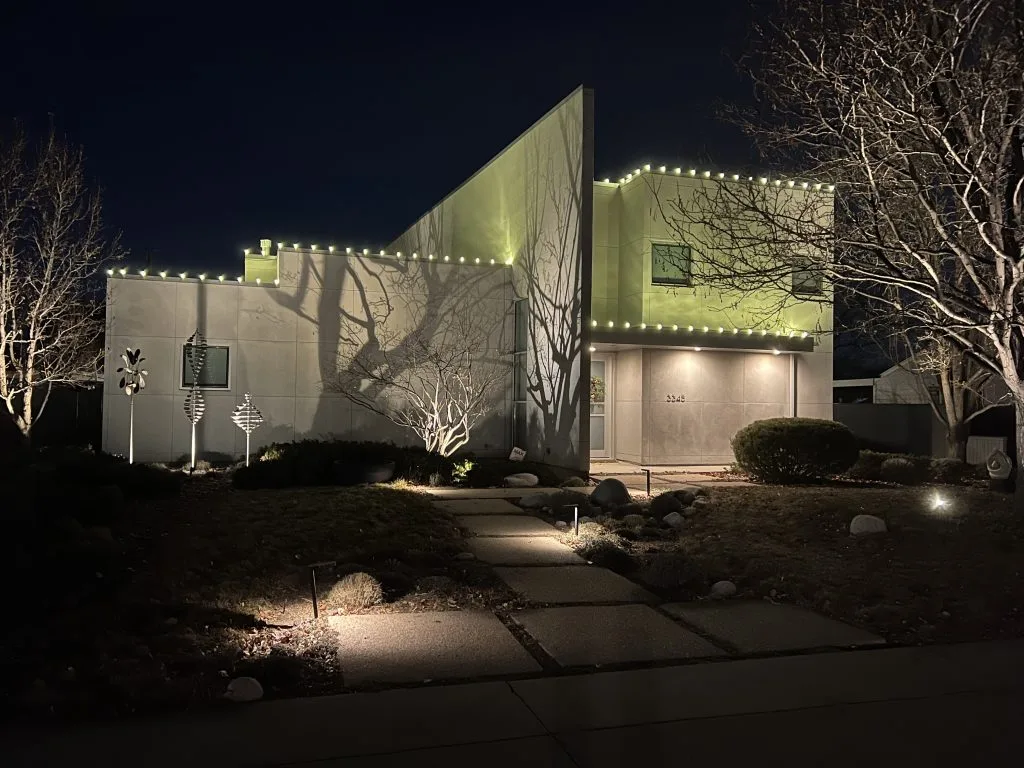 A modern house is illuminated with decorative lights, casting intriguing shadows at night