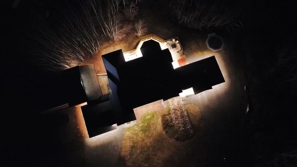 A dark aerial view highlights a house illuminated by surrounding lights