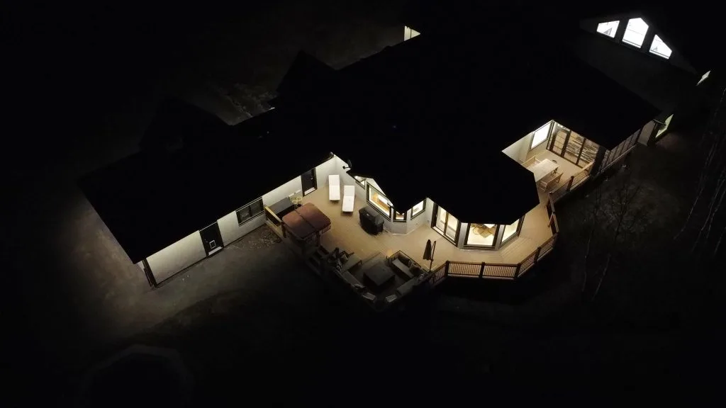 A well-lit house stands out against the dark night, surrounded by shadows