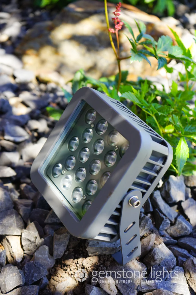 A rectangular light fixture sits on gravel near green plants and rocks