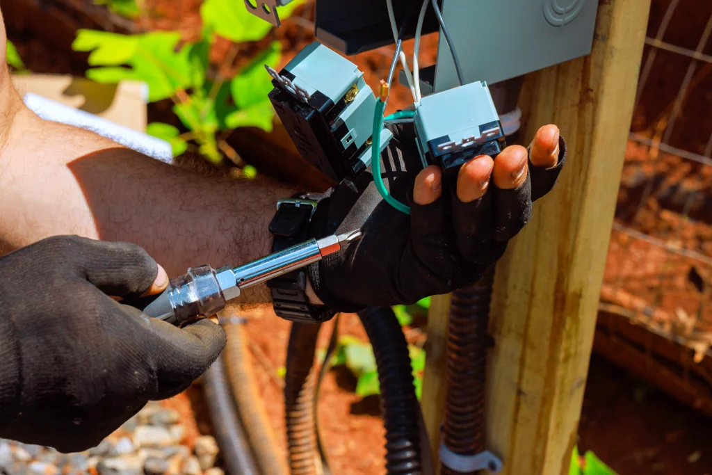 A person wearing gloves uses a tool to work on electrical connections